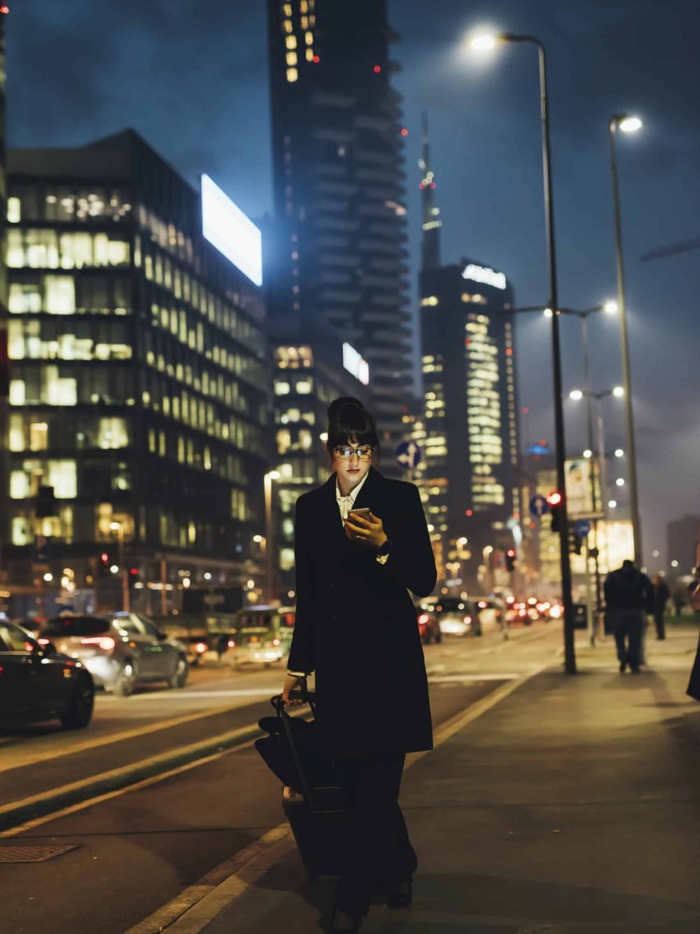Businesswoman using mobile phone and pulling trolley luggage, Milan, Italy